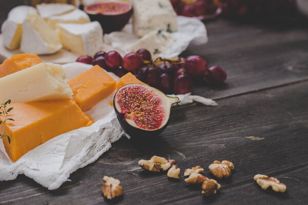 Various types of cheese with fruits and nuts on the wooden dark table. Selective focus