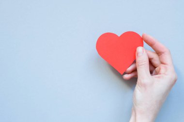 Mavi arka plan üzerinde kırmızı kağıt kalp tutan el. Kopya alanı ile