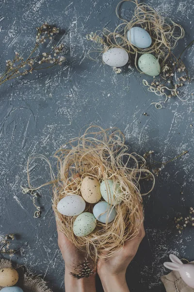 Vrolijk Pasen. Handen met Pasen eieren in nest met Pasen decoratie, bovenaanzicht — Stockfoto