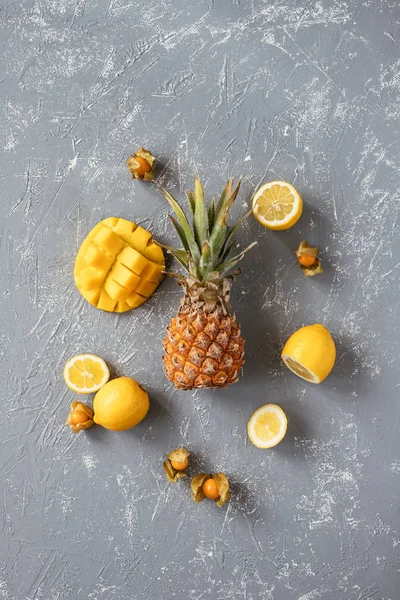 Yellow fruits. Ripe juicy pineapple with mango, physalis and lemons on gray wooden table, top view