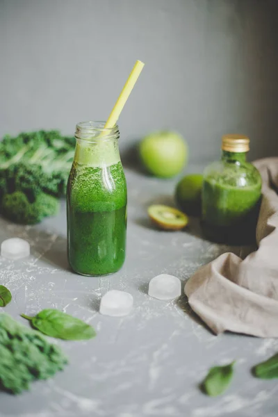 Healthy green smoothie with ingredients and ice cubes on gray background — Stock Photo, Image