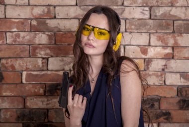 gözlük ve kulaklıklar bir tuğla duvar arka plan giyen güzel, Genç kız, elinde bir silahla