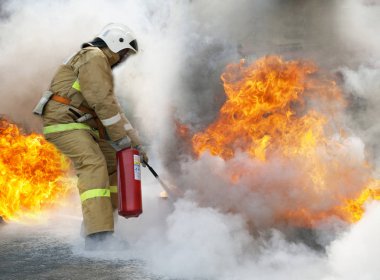 Büyük bir yangın söndürme. Profesyonel itfaiyeci özel takım elbiseli bir yangın söndürücü ile açık bir yangın söndürür.