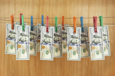 Yüz dolarlık banknotlar ahşap bir duvarın arkasındaki mandallara asılıyor.