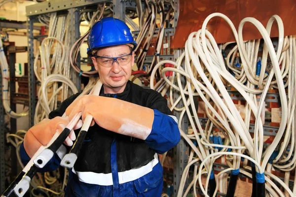 electromechanic in electrical safety gloves holds power cable, cabling connection of high voltage power electric line in industrial distribution fuseboard.