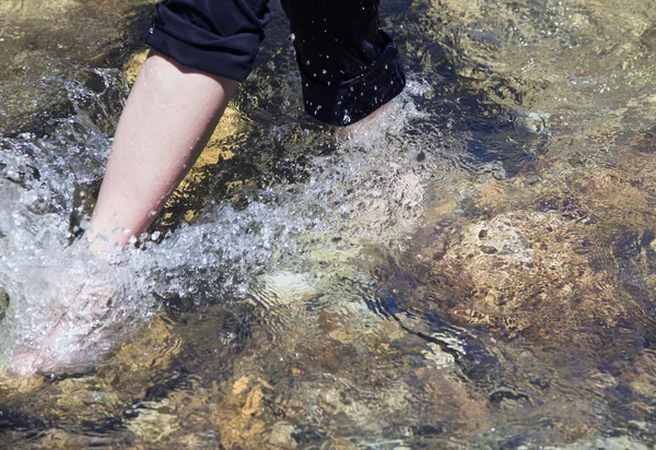 Female legs cross transparent mountain stream barefoot