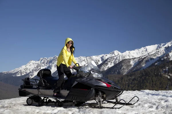 Girl on a snowmobile on a background of mountains