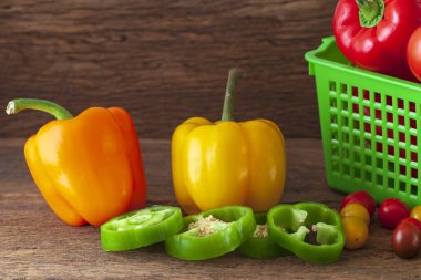 Üç büyük biber farklı renklerde kırmızı, sarı ve turuncu, ahşap bir arka planda.