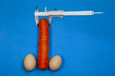 Erkek penisinin ve ameliyatının artması, erkek organının artması, iki yumurta ve siyah arka planda bir kalibre ile havuç,
