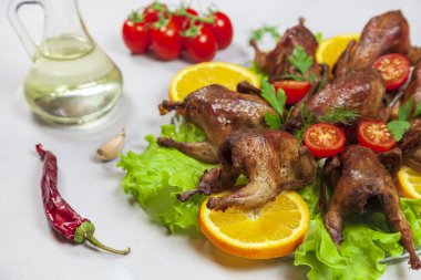 Turuncu üzerine kızarmış bıldırcın leşi, domatesli ve taze maydanozlu gri arka planda.