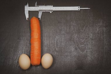 Erkek penisinin ve ameliyatının artması, erkek organının artması, iki yumurta ve siyah arka planda bir kalibre ile havuç,
