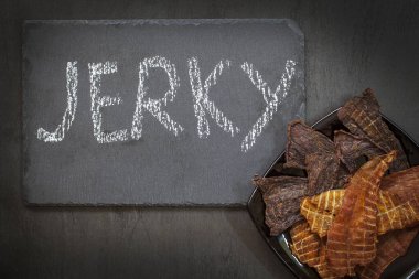 Biftek, tavuk ve hindi eti siyah arka planda bir tabakta, tebeşirle yazılmış kurutulmuş et, yukarıdan görünüm