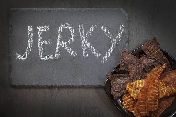 Rundvlees Kip Turkije Jerky Een Bord Een Zwarte Achtergrond Inscriptie — Stockfoto