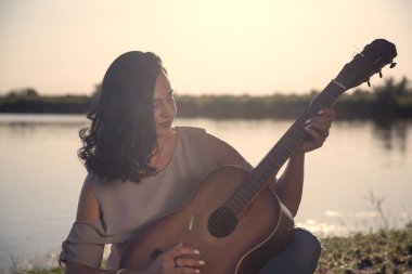 Yaz mevsimi, tatil, hafta sonu kızı, esmer göl kenarında gitarla yatıyor.