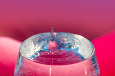 Cam bir makroda su damlası, yakın plan, pembe arka plan.