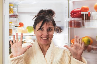 Bornozlu güzel esmer, geceleri buzdolabının yanında yemek yemek üzere.