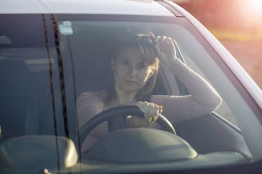 Gözlüklü güzel bir kadın beyaz bir geçitte araba kullanıyor.