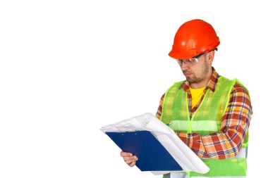 İnşaatçı, ustabaşı, koruyucu giysiler içinde, bir kask, yansıtıcı ceket ve gözlük, beyaz duvar arka planındaki çizimlere ve şemalara bakıyor, izole edilmiş.