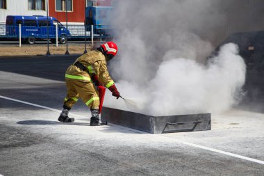 Büyük bir yangını söndürmek. Özel takım elbiseli profesyonel bir itfaiyeci yangın söndürücüyle yangını söndürüyor. İtfaiyecileri yangını söndürmek için eğitiyorum.