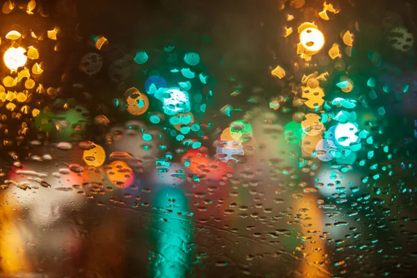 Rainy weather, night city, raindrops through the glass, abstract background from the light of cars and traffic lights, defocus, rain drops on car glass in rainy night