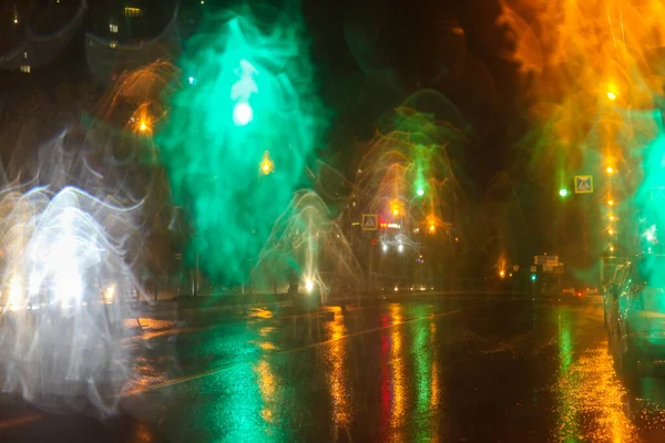 Rainy weather, night city, raindrops through the glass, abstract background from the light of cars and traffic lights, defocus, rain drops on car glass in rainy night