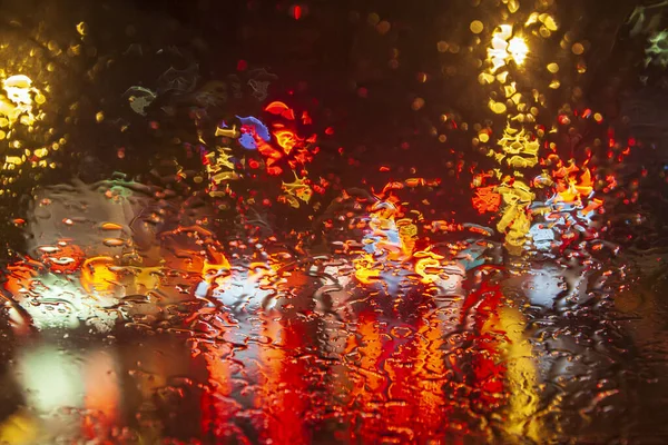 Rainy weather, night city, raindrops through the glass, abstract background from the light of cars and traffic lights, defocus, rain drops on car glass in rainy night