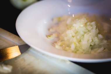 Kadın beyaz plastik bir tahtanın üzerinde soğan kesiyor. 