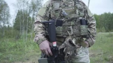 Ordu üniforması ve şapkalı ordu, orman ve çimenlerin arka planı üzerinde bir tarlada duruyor. Silahlı asker