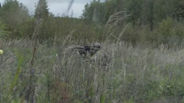 Elinde silah olan asker çimlerin üzerine gider. Askeri bir silahla sahada hareket ediyor