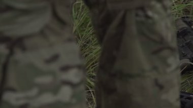 Askerlerin bacaklarının yanında çimenlerin üzerinde yatan askeri silah