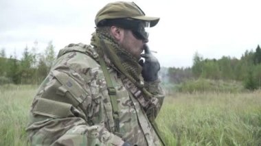 Tribünlerdeki asker ve orman arka planında sigara içiyor.