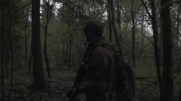 Soldier with a gun in his hand goes through the dark forest — Stockvideo