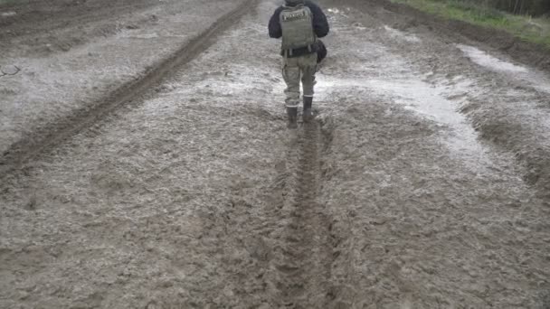 Girl in a military uniform and boots goes on a dirt road with a backpack — Stock Video