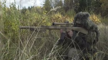Koruyucu kıyafetli bir alana oturan keskin nişancı tüfeği