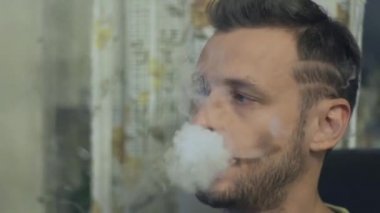 Genç adam bir masada oturur ve elektronik sigara içiyor, çiftler sağlar