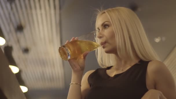 Junge blonde Frau trinkt ein Glas Bier in einer Bar — Stockvideo