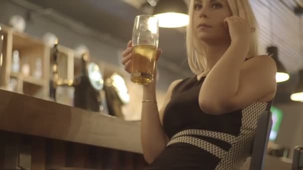 Giovane donna bionda che beve un bicchiere di birra in un bar — Video Stock