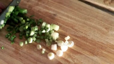 Kadının demet yeşil soğan ahşap tahta üzerinde bıçakla kesip. Malzemeler salata