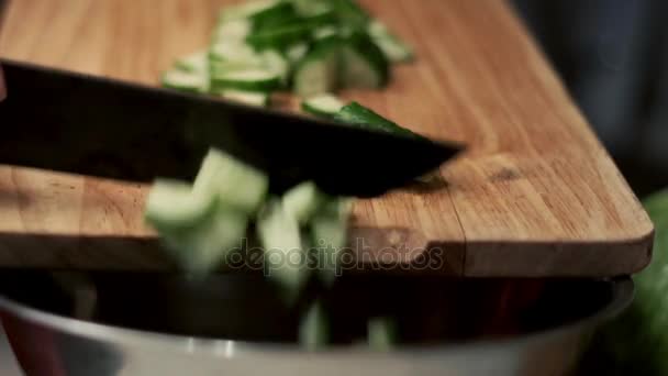 Knife pushes cut pieces of cucumber from wooden board with bowl — Stock Video