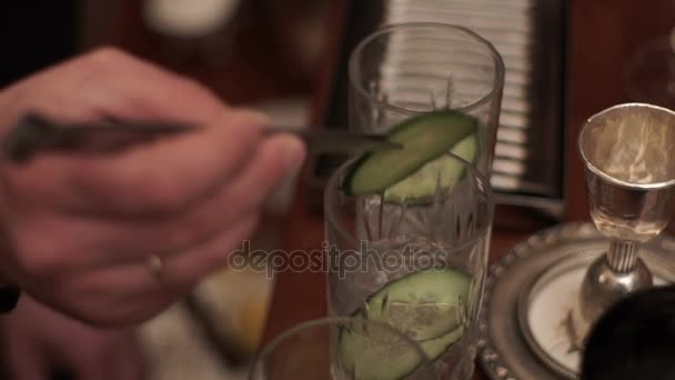 Bartendern sätter en bit gurka i glas. Cocktail förberedelse i bar med gurka — Stockvideo