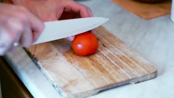 Hombre corta tomate con cuchillo sobre tabla de madera. Ensalada de preparación con tomates — Vídeos de Stock