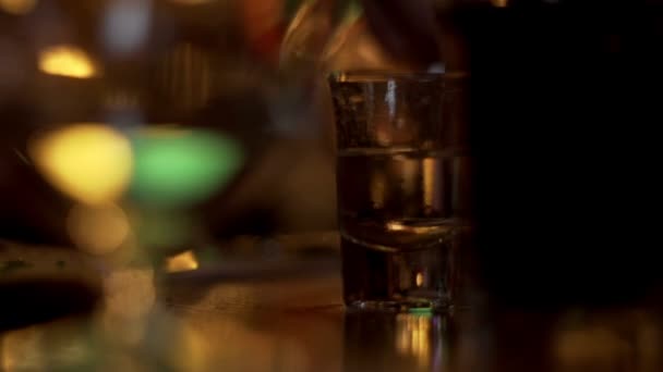 Close-up van glas met wodka staande geschoten op tabel op de achtergrond gieten mannenhand — Stockvideo