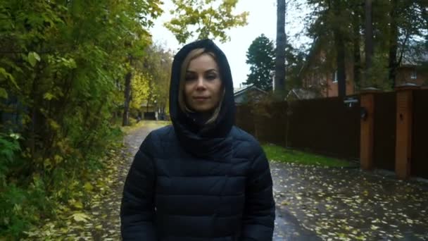 Портрет женщины в черной куртке с капюшоном, идущей по тропинке осенью — стоковое видео