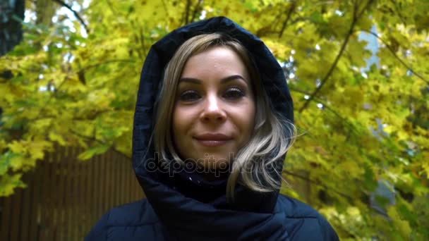 Крупным планом молодая женщина в черной куртке с капюшоном на фоне осени природы — стоковое видео