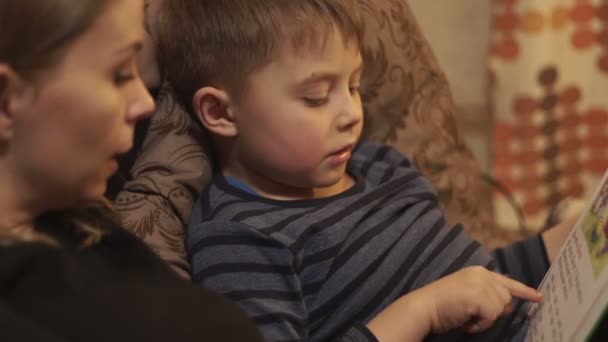 Junge Mutter zusammen kleiner Sohn liest ein Buch auf dem Bett liegend im gemütlichen Schlafzimmer — Stockvideo