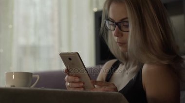 Kahve Kupası ayakta masada ile cep telefonuyla gözlüklü genç kadın