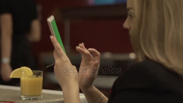 Mujer sonriente tocando en el teléfono móvil de pantalla verde en el zumo de naranja de fondo — Vídeos de Stock