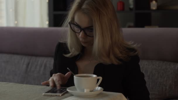 Beautiful woman typing message on screen mobile phone on background coffee cup — Stock Video