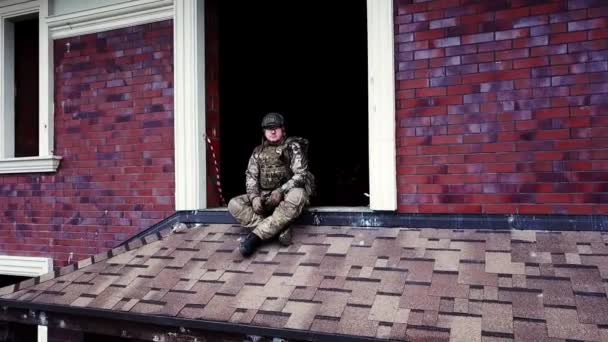 Drone view military soldier sitting on roof destroyed building in cottage village — Stock Video