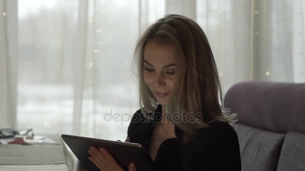 Mujer sonriente mirando en la tableta de la pantalla PC sentado en la mesa en la cafetería — Vídeo de stock